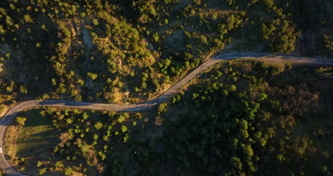 Aerial top-down drone follow shot capturing a group of cyclists navigating the winding descent from Mirador de Fuebla toward medieval town of A&iacute;nsa, nestled in the foothills of the Spanish Pyrenees