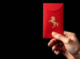 Hand holding red envelope with golden horse emblem against isolated black background for Year of the Horse.