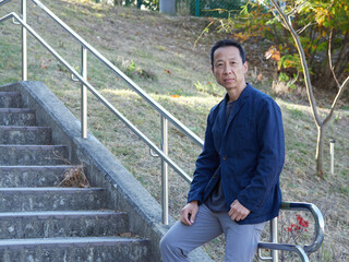 秋の昼の住宅地の公園の階段で休憩する一人の中年男性の姿