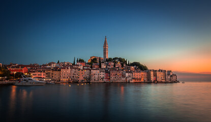 Fototapeta premium Rovinj, Croatia - Sunset view of beautiful Old Town of Rovinj with the tower of Saint Euphemia church in Adriatic sea coast. Clear blue sky, golden sunset colours