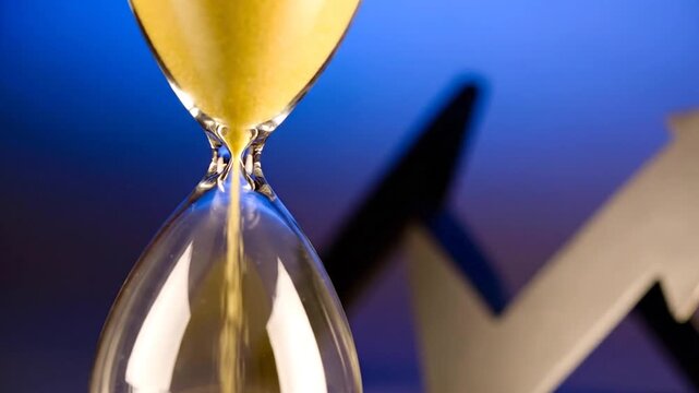Close-up of an hourglass with yellow sand flowing, backdrop has a dark arrow pointing upward