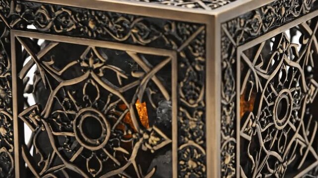A close-up shot of an intricately decorated bronze cube with an illuminated interior