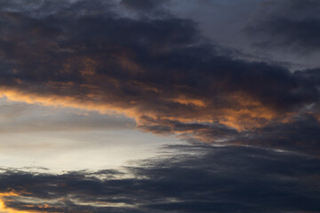 Dramatic sky with dark storm clouds and golden light creating ominous atmosphere for weather forecast background