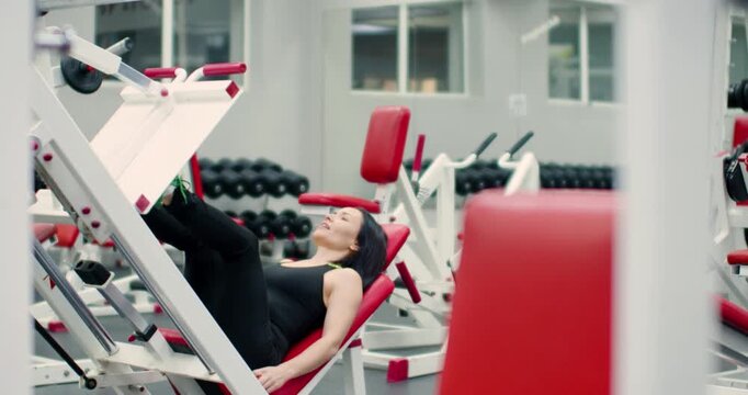 Gym workout. 4k footage of a middle-aged woman trains her leg muscles with controlled reps on the leg press machine, focusing on strength. Slow motion video.