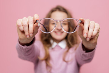 Clear eyeglasses held in hands with smiling woman blurred on pink background