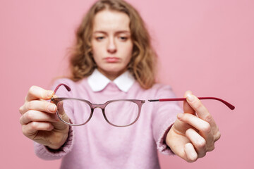 Broken eyeglasses in hands with detached temple arm and sad woman on pink background