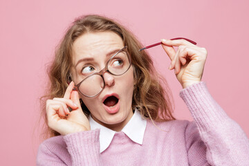 Surprised woman with crooked broken glasses holding snapped temple arm on pink background