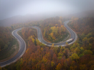 Aerial view of a single car driving on a winding foggy mountain road at sunrise