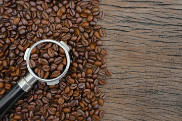  top view of coffee beans in a portafilter, with a background of roasted coffee beans on an old wooden table.