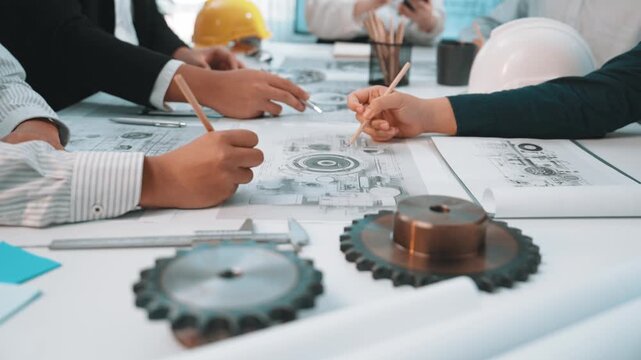 A collaborative engineering team reviews technical drawings while examining gear components in a modern office. The image captures teamwork and innovation in action. SACTR