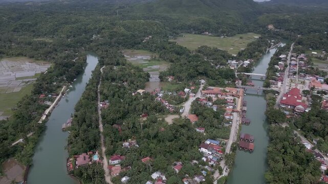 Aerial drone backward reveal of Loboc River and village in Bohol, Philippines. Aerial drone footage flying backward to gradually reveal the Loboc River and the riverside village in Bohol, Philippines.