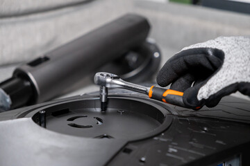 Gloved hand skillfully using a ratchet wrench to tighten components on an electronic device, highlighting precision, assembly, repair, and technical service