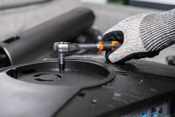 Gloved hand meticulously using a ratchet wrench to assemble a modern computer monitor, symbolizing professional repair and technical service