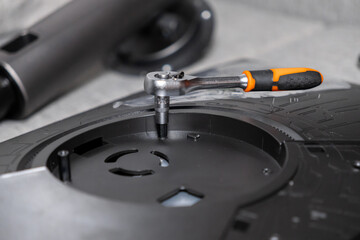 Ergonomic chrome ratchet wrench with orange rubberized handle carefully turning a screw on a textured black electronic component, signifying precise repair