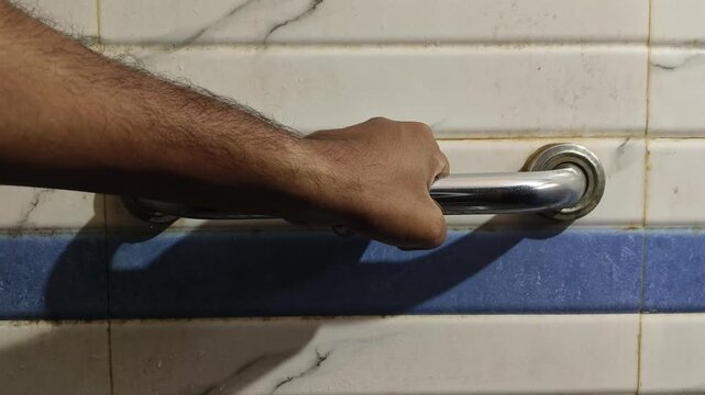 Adult person hands holding on to a safety bar next to the toilet in the bathroom. Man with disability problems. Concept of objects to facilitate the daily life of people with disabilities.