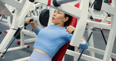 Gym workout. Bench press in hammer machine. A Caucasian woman trains her chest muscles with focused...