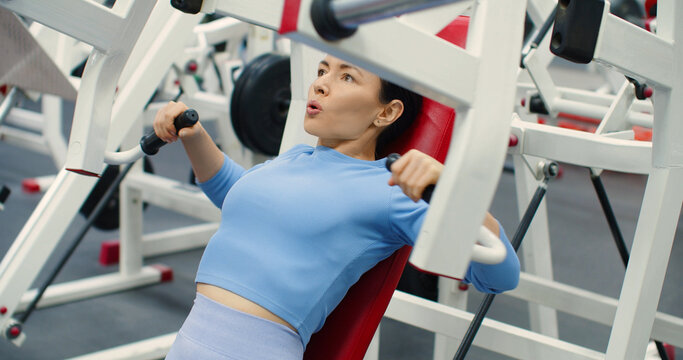 Gym workout. Bench press in hammer machine. A Caucasian woman trains her chest muscles with focused bench press reps on the hammer machine during an intense gym workout.