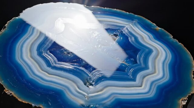 Extreme slow motion rotation of a massive highly polished blue agate slice reflecting light spectacularly across its banded structure detail, glossy, refraction