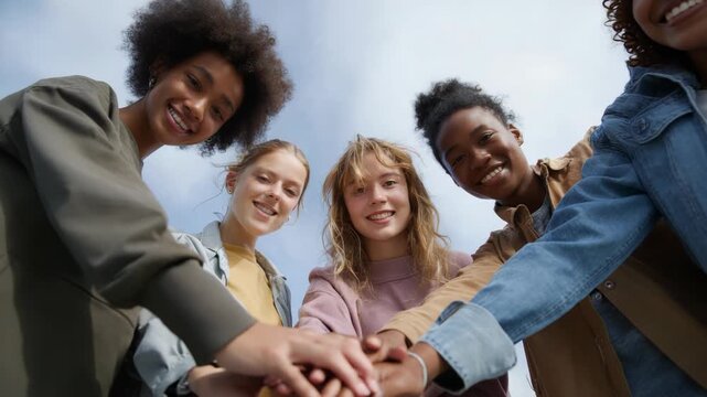 Diverse group of friends smiling and holding hands outdoors under a blue sky