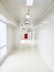 A bright, sterile white hallway with fluorescent lights and a red fire extinguisher cabinet at the end.