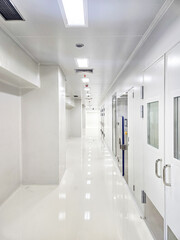 A long, clean, white corridor with doors on the right side and lights on the ceiling.