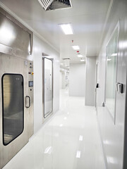 Cleanroom corridor with sterile white walls, stainless steel doors, and bright overhead lighting.
