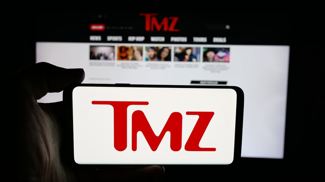 Stuttgart, Germany - 12-12-2025: Person holding cellphone with logo of US tabloid news company TMZ on screen in front of webpage. Focus on phone display.