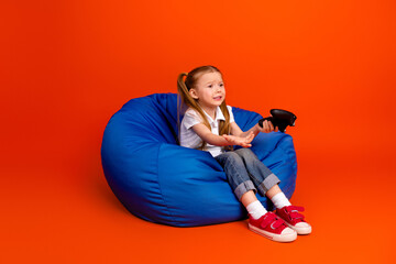 Young girl sits on a blue bean bag holding a game controller smiles during playtime conveying joy and casual home leisure