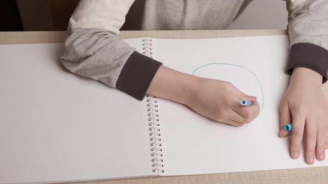 A student draws a little man's face with a felt-tip pen on a white sheet.