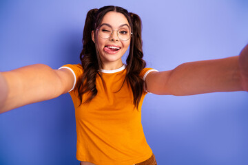 Selfie of a happy young girl in orange t shirt with glasses taking a playful photo against a purple background for fashion lifestyle and advertising use