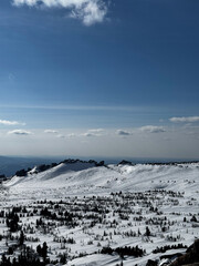Wide snowy mountain view with blue sky and rocky peaks in winter.