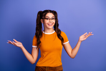 Young female student with playful braids wearing an orange shirt stands against a violet blue...