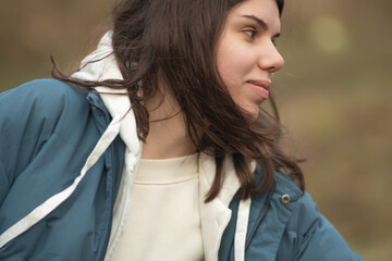 Young woman with long dark hair wearing a blue puffer jacket and gray sweatpants is walking a dog along a rural path surrounded by tall grass and trees in the background