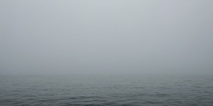 Nebel &uuml;ber dem ruhigen Meer mit verschwommener K&uuml;ste und sanften Wellen in grauer Stimmung