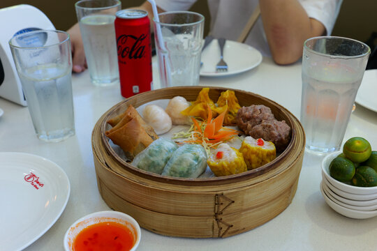 Marilao, Bulacan Philippines - November 2, 2025: Assorted Chinese dim sum served in a traditional bamboo steamer with dumplings and chilled Coca Cola on a restaurant table.
