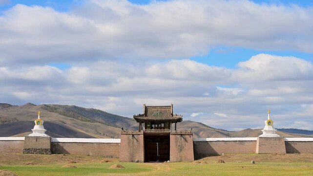 Wide shot of a gate and the white stupa wall surrounding Erdene Zuu in Kharkhorin, Mongolia. The ancient Buddhist temple complex seen from the grassy steppe.