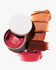 Cosmetic cream makeup product swatches demonstrating rich vibrant shades of berry and bronze highlights against white