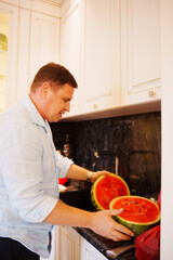 Man cuts watermelon in a kitchen area during daytime