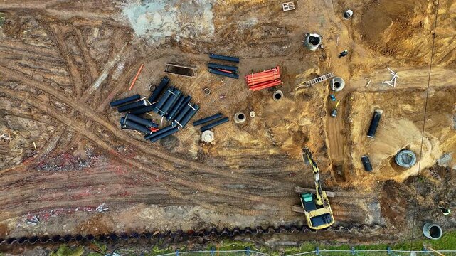 Working excavator on construction site with underground pipelines, trenches and infrastructure aerial top view