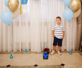 Boy stands next to balloons and toy truck at party