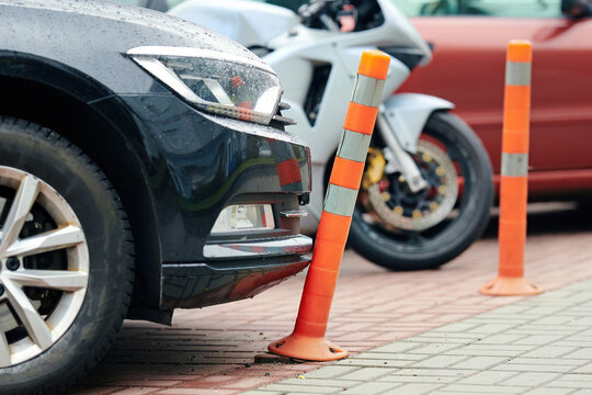 Car bumper touching flexible plastic bollard on parking lot, minor contact, damage to reflective warning post, everyday parking incidents and traffic safety infrastructure. Bumper contact warning post