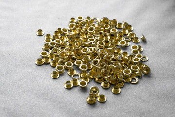 Gold metal eyelets scattered on a gray surface for sewing projects  