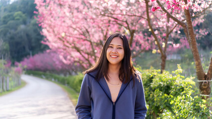 A young woman is standing amidst the cherry blossom trees.