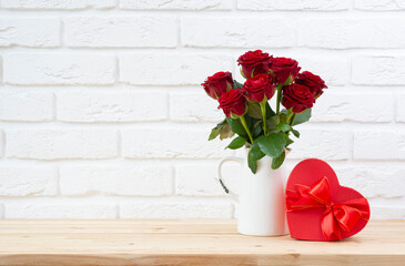 Happy Valentines day concept with red rose flowers and heart shape gift box on wooden table over white brick wall background