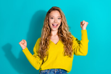 Young woman celebrates success in bright yellow sweater against blue background and happy smile