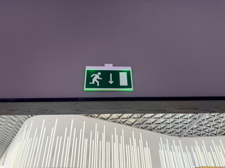 Follow exit sign. Illuminated sign on wall with symbol of person running out. Green board with white symbol and exit arrow in case of building fire. Indoor safety concept and news