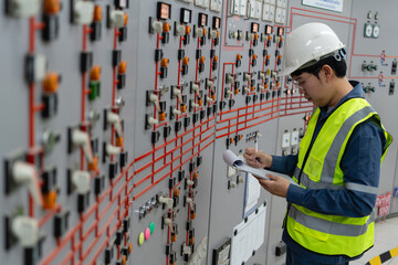 Electrical engineer inspecting control panel in industrial power facility, documenting system status for safety compliance, preventive maintenance, and operational reliability in modern room