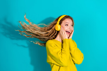 Young woman in yellow sweater wearing headphones smiles against blue background a bright fashion...