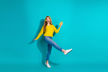 Young woman in yellow sweater jumps with phone against blue background for fashion lifestyle stock...