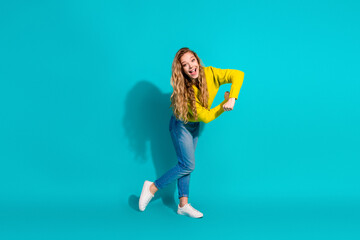 Young woman in yellow sweater dances playfully against bright blue background for a lively...